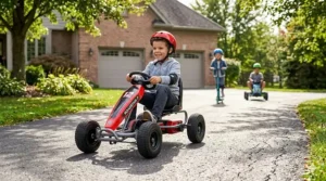A 7-year-old boy driving a red electric go-kart on a driveway.
