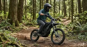 A teenage boy riding a powerful electric dirt bike through a dirt trail in the woods.