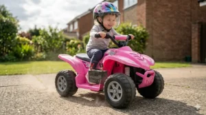 A young child riding a pink toddler quad powered by a rechargeable 6v battery on a paved driveway.