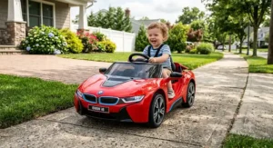 Happy toddler driving a red BMW i8 ride-on car on a sunny sidewalk.