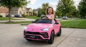 A young girl smiling inside a pink Lamborghini Urus electric ride-on car for kids with LED headlights on.