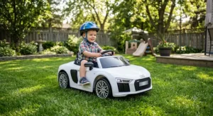 Young toddler wearing a safety helmet driving a white 12V Audi R8 ride on car on a backyard lawn