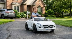 Toddler enjoying a white 12-volt Mercedes-Benz SLS ride-on car with realistic LED headlights outdoors.