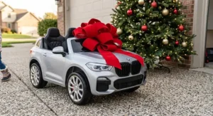 A silver 2 seater luxury ride on car for toddlers topped with a giant red bow next to a Christmas tree