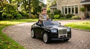 Young child driving a sleek black Rolls Royce ride-on car on a paved driveway outdoors
