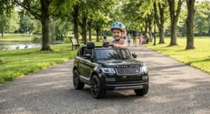 Young child wearing a helmet driving a black 24V Range Rover ride-on car on a park pathway.