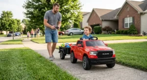 A parent using a remote control to guide a Ram truck ride-on toy with a trailer on the sidewalk.