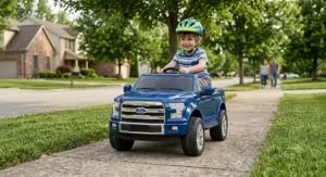 Young boy wearing a helmet riding a blue Ford F150 toy truck down a neighborhood sidewalk.