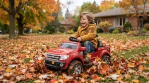 An all-terrain ride-on car for 5 year old driving through fallen autumn leaves in a yard.