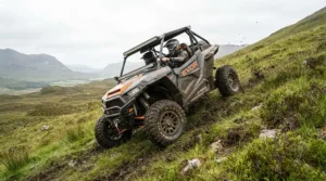 An off-road electric vehicle for adults tackling a steep grassy hill climb in a rural field.